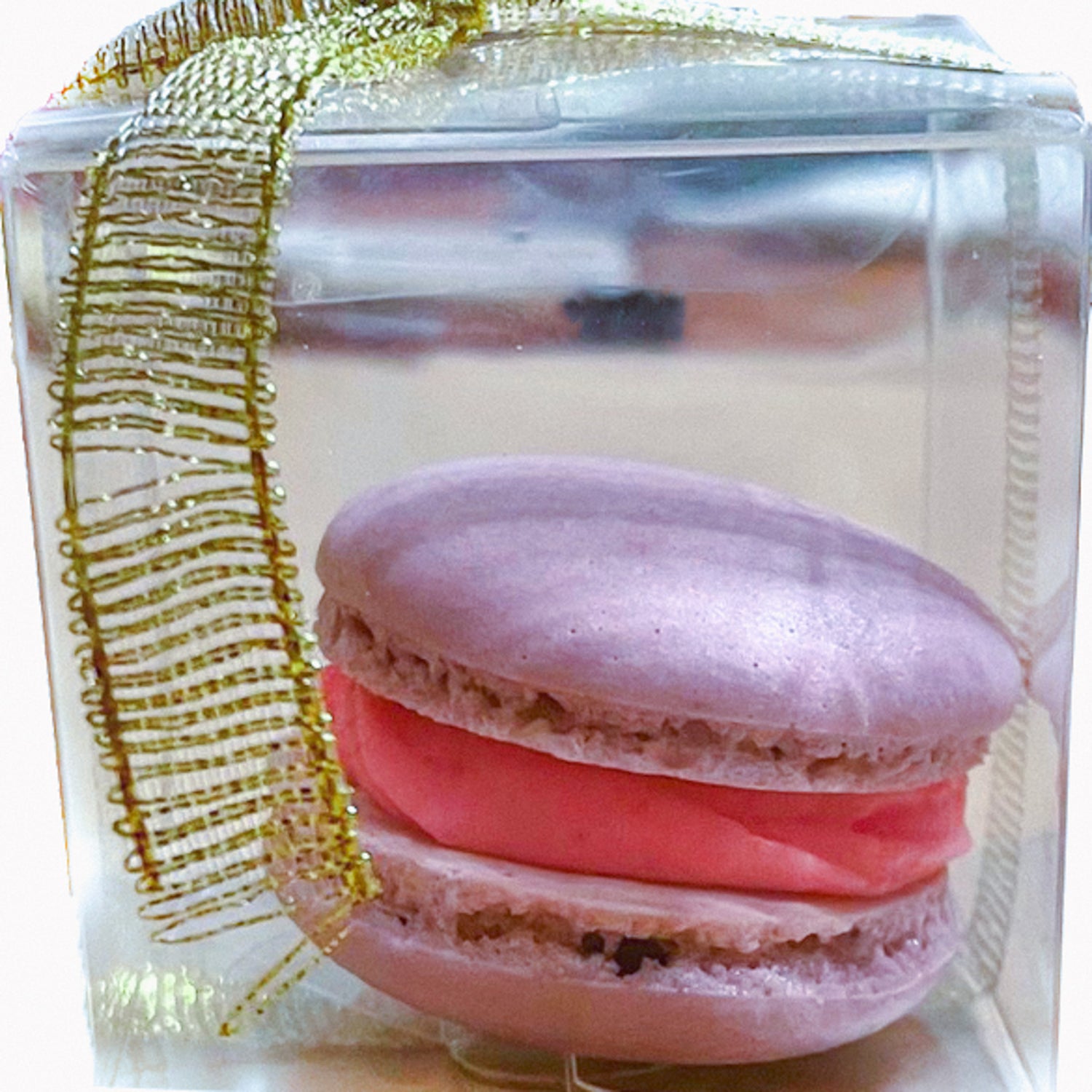 Pink macaron with pink filling individually wrapped in a clear box with a gold bow